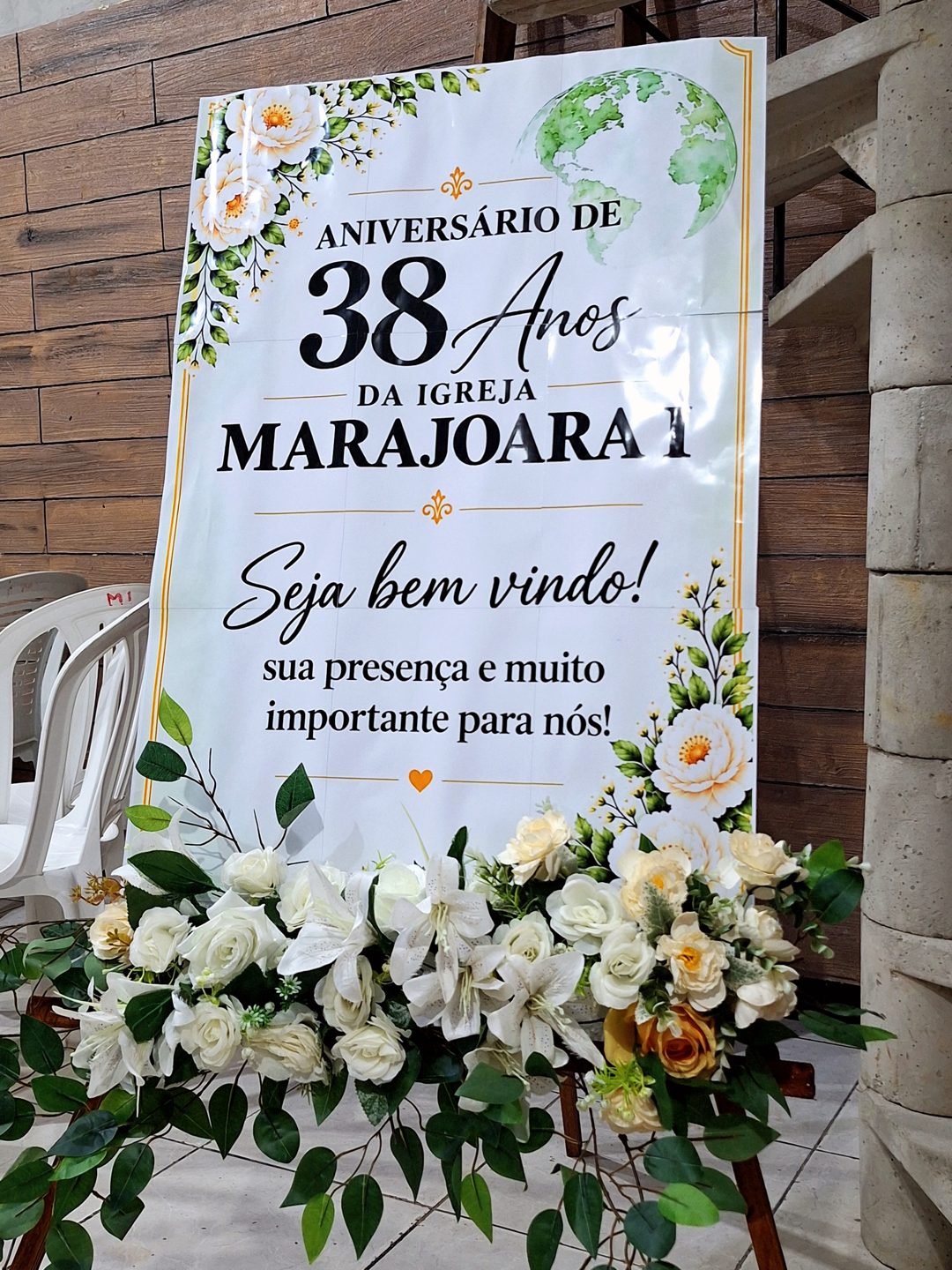 Placa de boas-vindas dos 38 anos da igreja com arranjo de flores